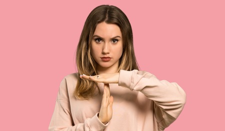 Teenager girl with pink sweater making time out gesture over isolated pink background