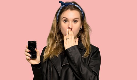 Teenager girl with leather jacket with a broken phone on isolated pink background