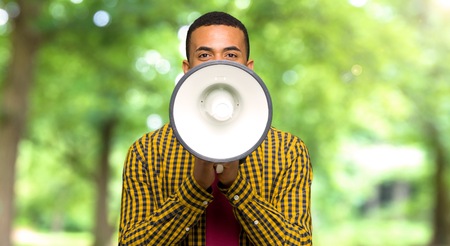 Young afro american man shouting through a megaphone to announce something in a parkの写真素材