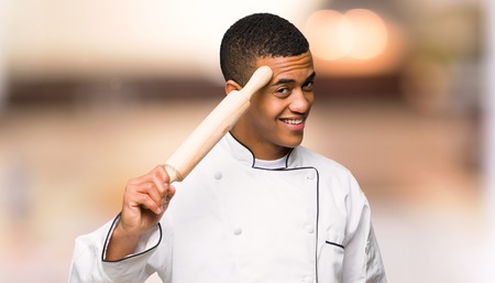 Young afro american chef man saluting with hand on unfocused backgroundの写真素材