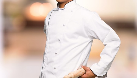 Young afro american chef man suffering from backache for having made an effort on unfocused backgroundの写真素材