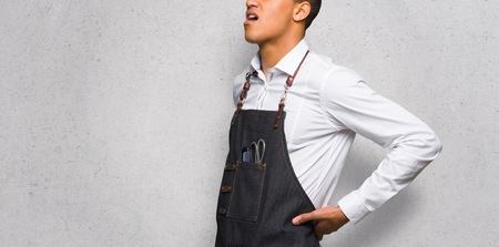 Young afro american barber man suffering from backache for having made an effort on textured wallの写真素材