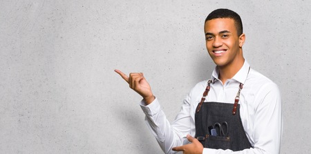 Young afro american barber man pointing finger to the side in lateral position on textured wallの写真素材
