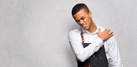 Young afro american barber man suffering from pain in shoulder for having made an effort on textured wallの写真素材