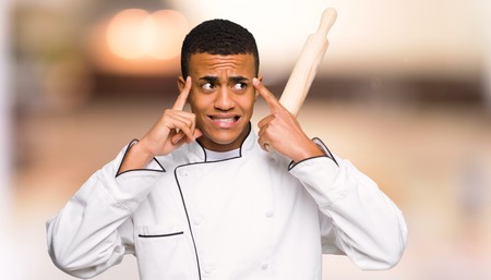 Young afro american chef man having doubts and thinking on unfocused backgroundの写真素材