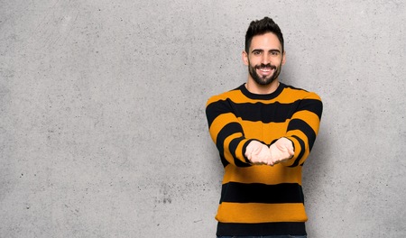 Handsome man with striped sweater holding copyspace imaginary on the palm to insert an ad over textured wallの写真素材