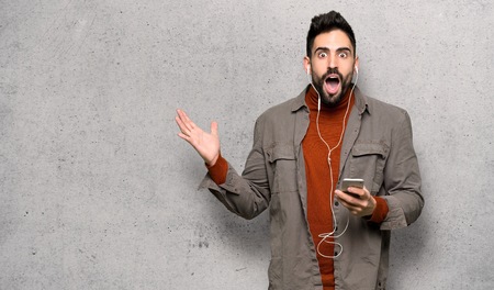 Handsome man with beard surprised and sending a message over textured wallの写真素材