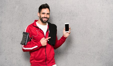 Handsome sportman happy and pointing the mobile over textured wallの写真素材