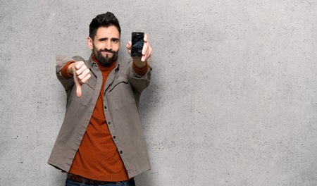 Handsome man with beard with troubled holding broken smartphone over textured wallの写真素材