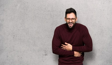 Handsome man with glasses smiling a lot while putting hands on chest over textured wallの写真素材