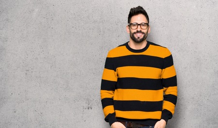 Handsome man with striped sweater with glasses and happy over textured wallの写真素材