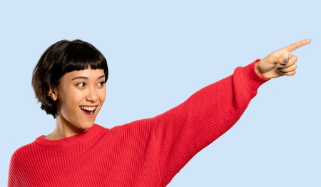 Short hair girl with red sweater pointing away on isolated blue backgroundの写真素材