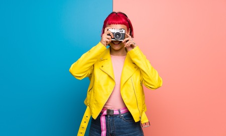 Young woman with yellow jacket holding a cameraの写真素材