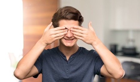 Teenager man covering eyes by hands. Surprised to see what is ahead at indoorsの写真素材