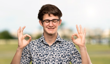 Teenager man with flower shirt and glasses in zen pose at outdoorsの写真素材