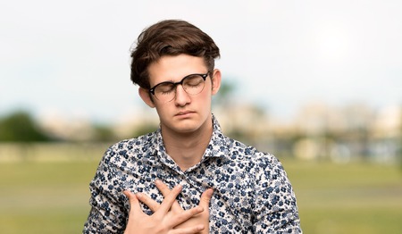 Teenager man with flower shirt and glasses having a pain in the heart at outdoorsの写真素材