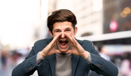 Teenager man with turtleneck shouting and announcing something at outdoorsの写真素材