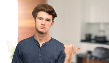 Teenager man unhappy and pointing to the side at indoorsの写真素材