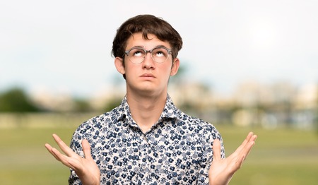 Teenager man with flower shirt and glasses frustrated by a bad situation at outdoorsの写真素材
