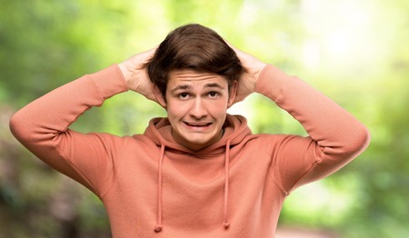 Teenager man with sweatshirt frustrated and takes hands on head at outdoorsの写真素材