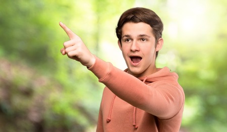 Teenager man with sweatshirt pointing away at outdoorsの写真素材