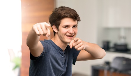 Teenager man points finger at you while smiling at indoorsの写真素材