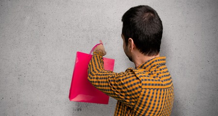 Man with shopping bags pointing back with the index finger over textured wallの写真素材