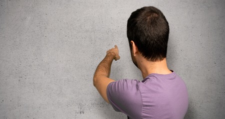 Handsome man pointing back with the index finger over textured wall