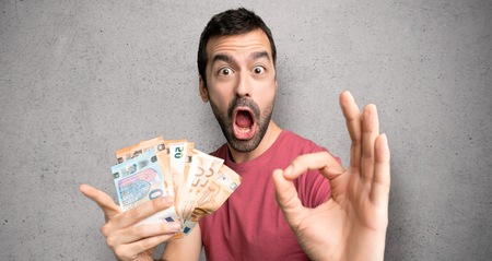 Man taking a lot of money showing ok sign with and giving a thumb up gesture over textured wall