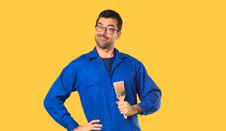 Painter man posing with arms at hip and smiling on isolated yellow backgroundの写真素材