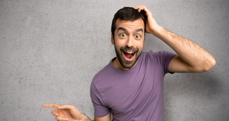 Handsome man pointing finger to the side and presenting a product over textured wall