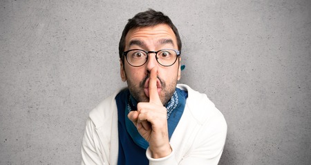 Handsome man with glasses showing a sign of silence gesture putting finger in mouth over textured wallの写真素材