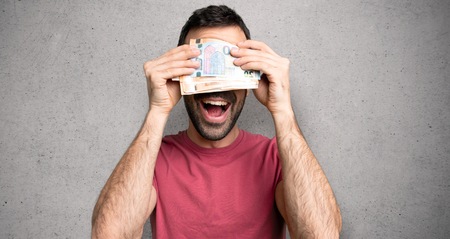 Man taking a lot of money covering eyes by hands. Surprised to see what is ahead over textured wallの写真素材