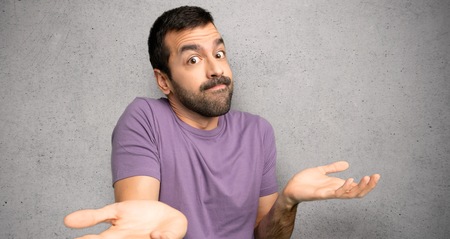 Handsome man making unimportant gesture while lifting the shoulders over textured wallの写真素材