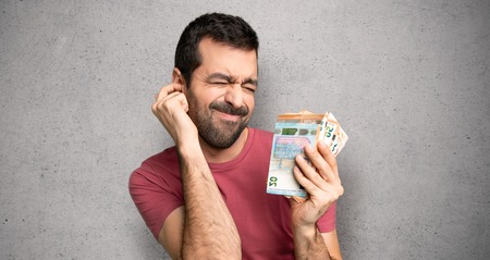 Man taking a lot of money covering ears with hands. Frustrated expression over textured wall