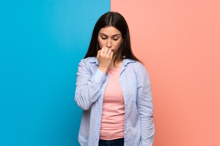 Young woman over pink and blue wall having doubtsの写真素材