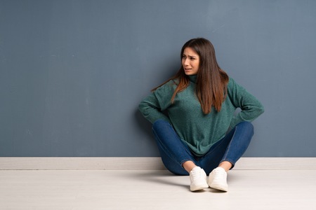 Young woman sitting on the floor suffering from backache for having made an effortの写真素材