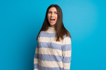 Young woman over blue wall shouting to the front with mouth wide openの写真素材