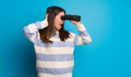 Young woman over blue wall and looking in the distance with binocularsの写真素材