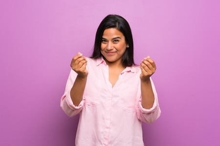 Young Colombian girl over purple wall making money gestureの写真素材