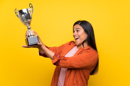 Young Colombian girl over yellow wall holding a trophyの写真素材