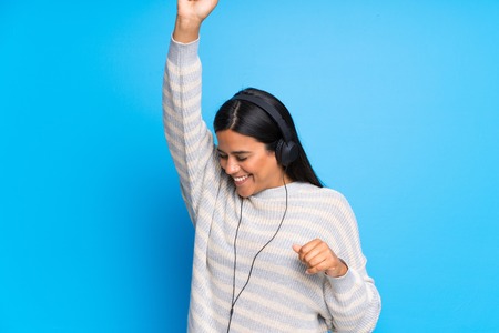 Young Colombian girl with sweater listening to music with headphones and dancingの写真素材