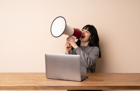 Young woman working with her laptop shouting through a megaphoneの写真素材