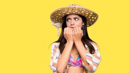 Teenager girl on summer vacation nervous and scared putting hands to mouth over isolated yellow backgroundの写真素材