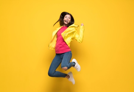 Teenager girl jumping over isolated yellow wallの写真素材