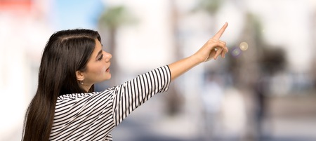 Teenager girl with striped shirt pointing away at outdoorsの写真素材