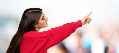 Teenager girl with red sweater pointing away at outdoorsの写真素材