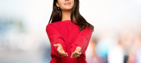 Teenager girl with red sweater holding copyspace imaginary on the palm to insert an ad at outdoorsの写真素材