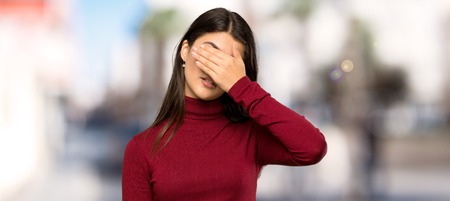 Teenager girl with turtleneck covering eyes by hands. Do not want to see something at outdoorsの写真素材