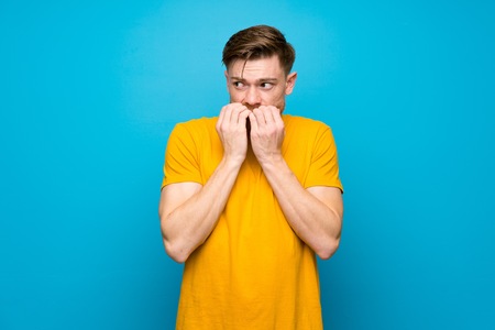 Redhead man over blue wall nervous and scared putting hands to mouthの写真素材